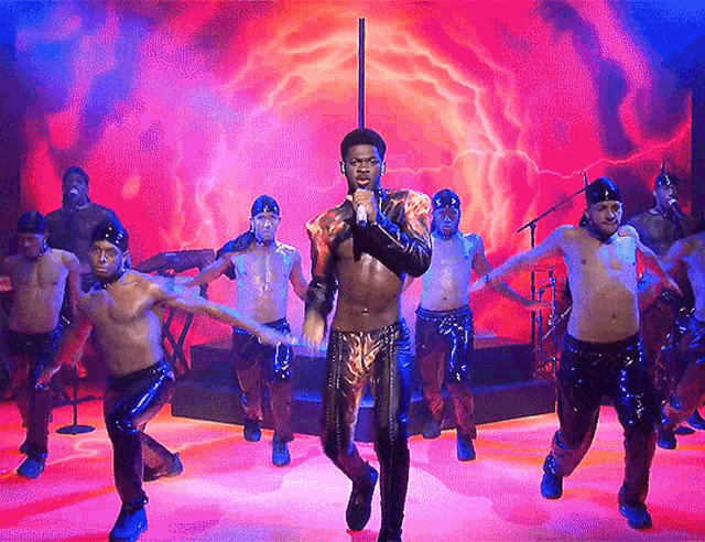 a man singing into a microphone with a group of men behind him