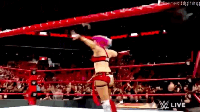 a woman with pink hair is standing in a wrestling ring with a crowd watching .