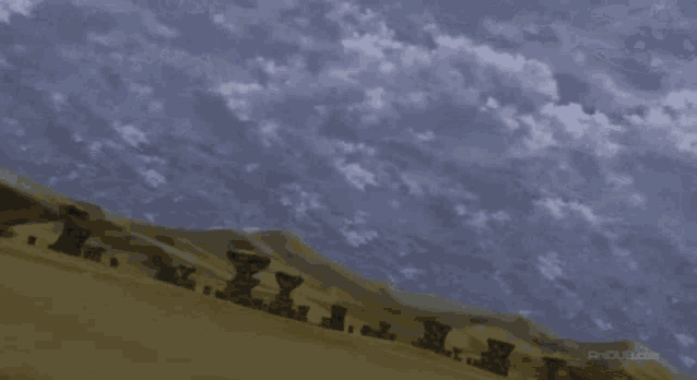 a large black object is flying through the sky over a desert landscape .