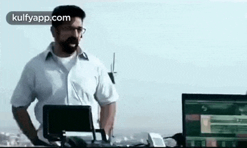 a man with a beard is standing in front of a computer monitor .