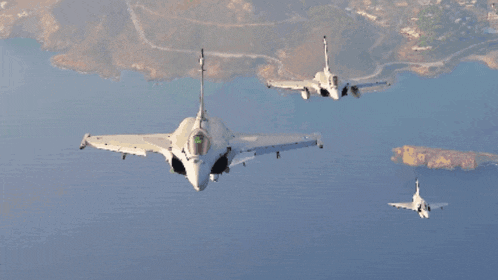 a group of fighter jets are flying in formation over a body of water