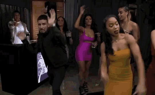 a group of people are dancing in a room while a man stands behind them .