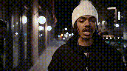 a man wearing a white hat and a black jacket is standing on a sidewalk .