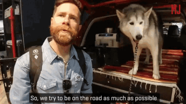 a man with a beard stands next to a husky dog and says " so we try to be on the road as much as possible "