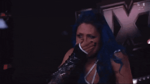 a woman with blue hair is crying in front of an x on a wall
