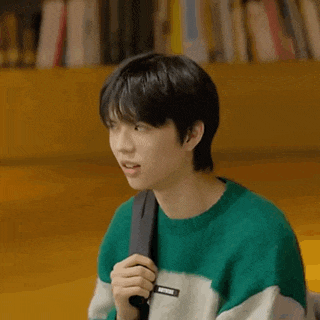 a young man wearing a green sweater and a black backpack is holding a microphone .