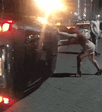 a woman pushes a car that has a license plate that says ' aa ' on it
