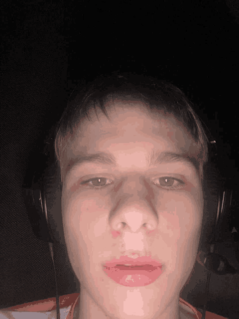 a young man wearing headphones looks at the camera with a red lip