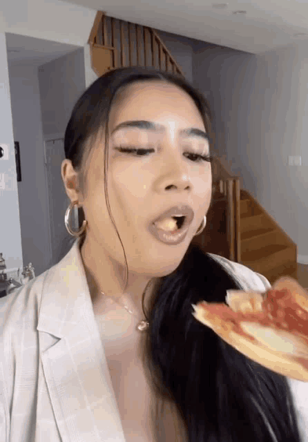 a woman is eating a slice of pizza in front of a staircase