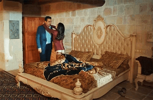 a man and a woman are standing next to a large bed