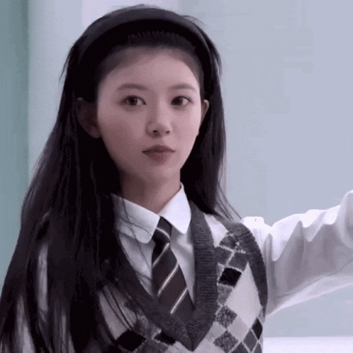 a girl with long black hair wearing a headband and a sweater vest and tie .