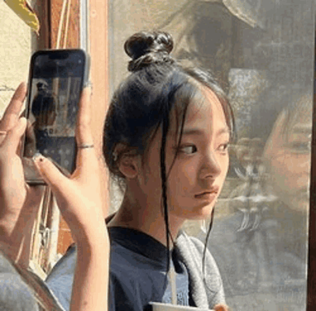a woman is taking a picture of herself with a cell phone in front of a window .