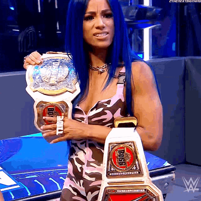 a woman with blue hair is holding a wrestling championship belt