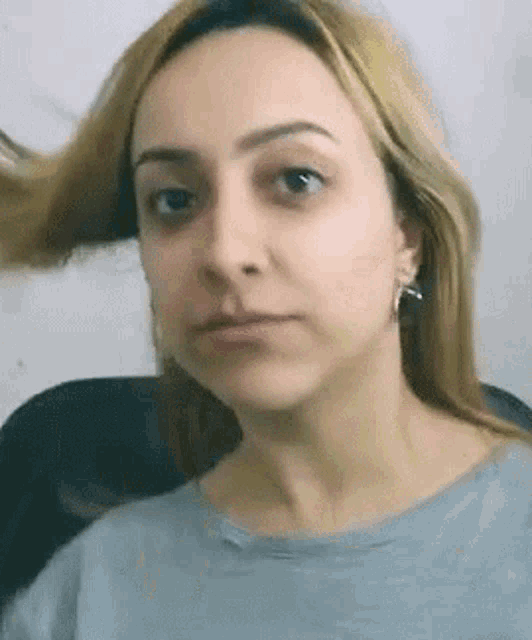 a woman with blonde hair is wearing a grey shirt and earrings