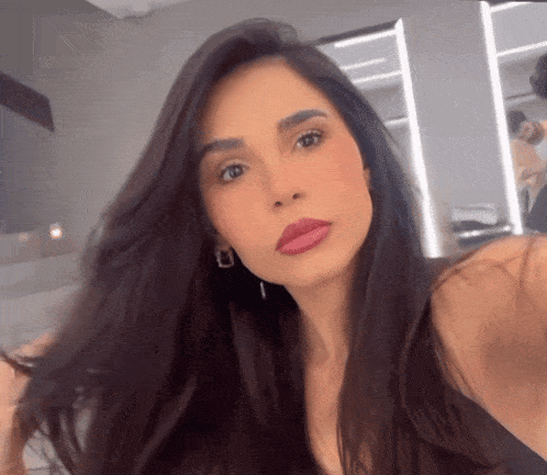 a woman with long dark hair and pink lips takes a selfie