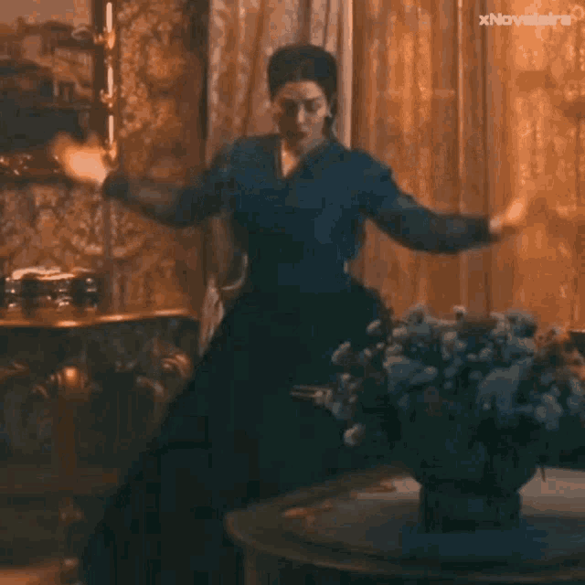 a woman in a blue dress is standing in front of a table with a vase of flowers on it .