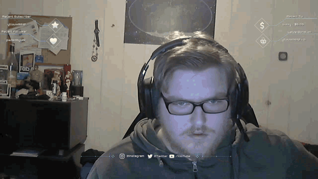 a man wearing glasses and headphones looks at the camera with a screen behind him that says recent subscriber