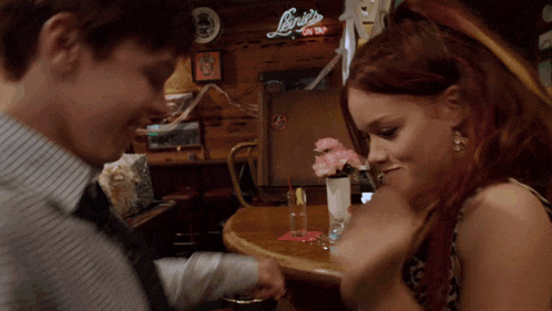 a man and a woman are sitting at a table in front of a sign that says ' linky 's on tap '