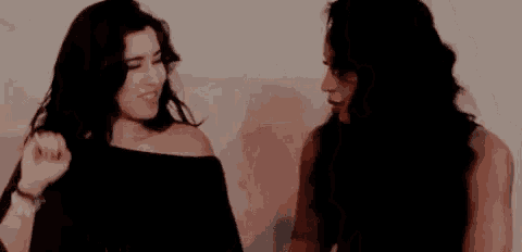 two women are standing next to each other and dancing in front of a wall .