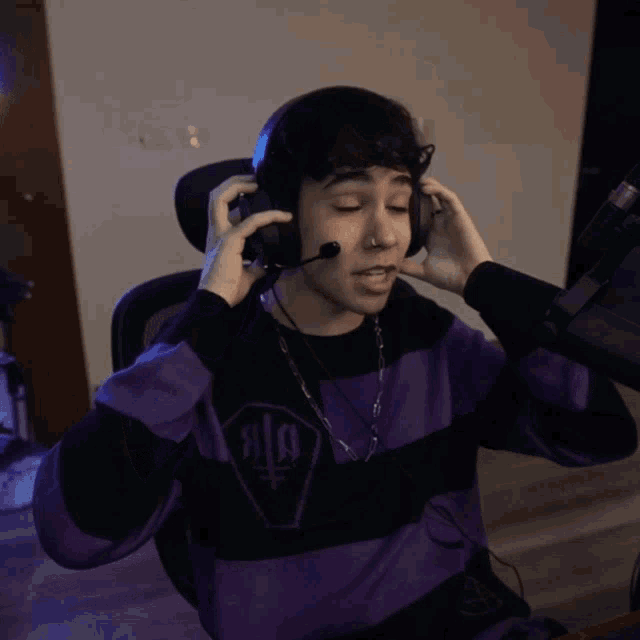 a man wearing headphones and a purple and black striped shirt is sitting in front of a microphone
