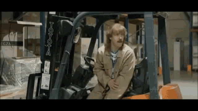 a man with a mullet is sitting in a toyota forklift .