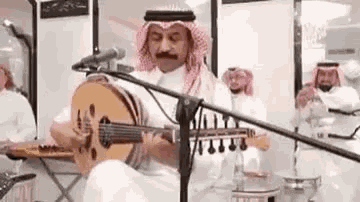a man is playing a guitar in front of a microphone while sitting on a stage .