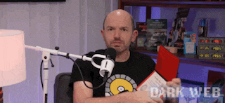 a man is sitting in front of a microphone and holding a red card with the words dark web on the bottom right