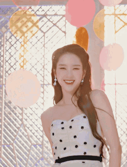 a woman in a white dress with black polka dots smiles in front of balloons