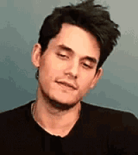 a close up of a man 's face with his eyes closed . he is wearing a black shirt and a necklace .