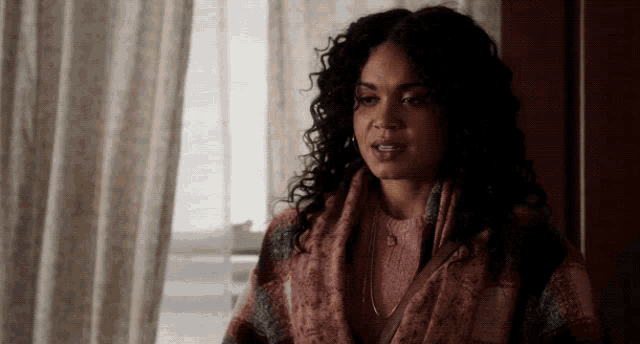 a woman with curly hair is wearing a pink sweater and a plaid scarf