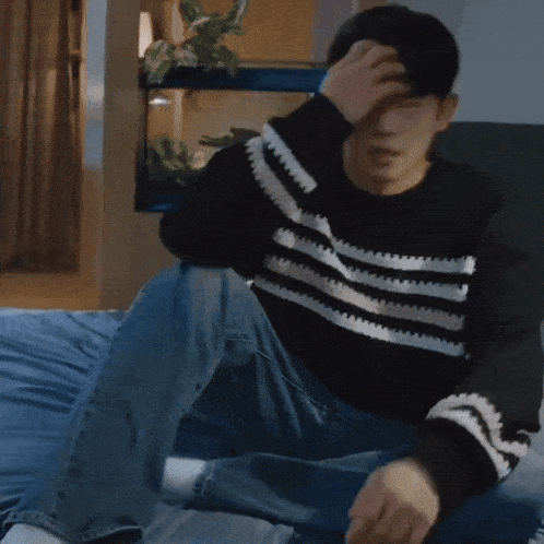 a man wearing a black and white striped sweater is sitting on a bed .
