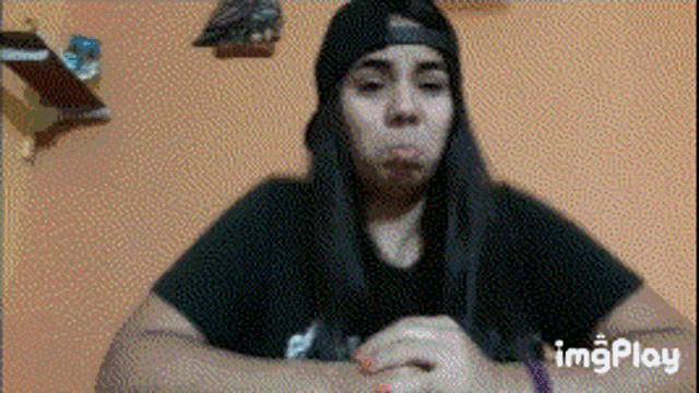 a girl wearing a beanie and a black shirt is sitting in front of an orange wall .