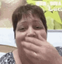 a woman is covering her mouth with her hand while looking at the camera .