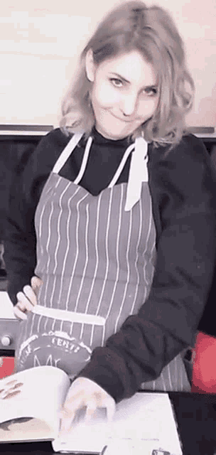 a woman wearing a striped apron is holding a book