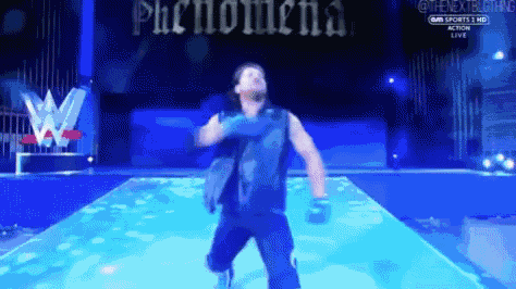 a man in a blue vest is standing on a stage with phenomena written on the screen behind him