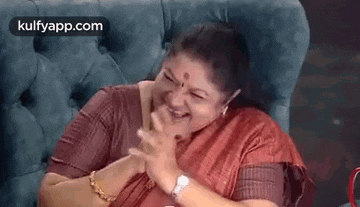 a woman is sitting in a chair and laughing with her hands on her chest .