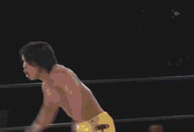 a wrestler in yellow pants is doing a handstand in a wrestling ring