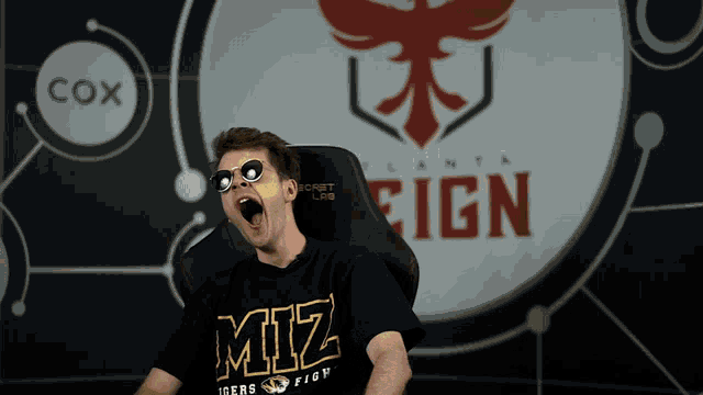 a man wearing a shirt that says miz is sitting in front of a sign