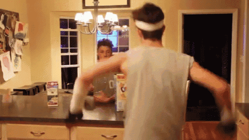 a man in a white tank top is standing in front of a kitchen counter looking at his reflection in a mirror