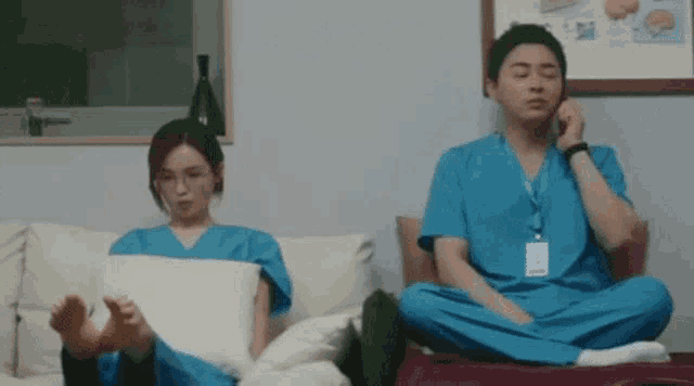a man and a woman in scrubs are sitting on a couch with their feet crossed .
