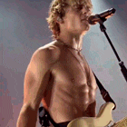 a shirtless man is holding a guitar and singing into a microphone .