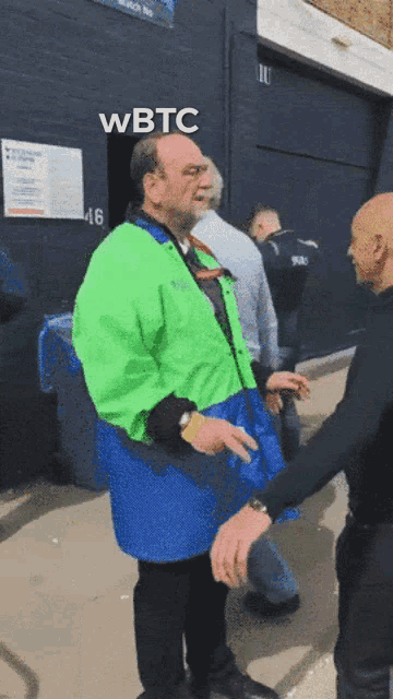 a man in a green and blue jacket talks to another man