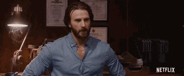 a man with a beard is sitting at a desk in front of a netflix sign .