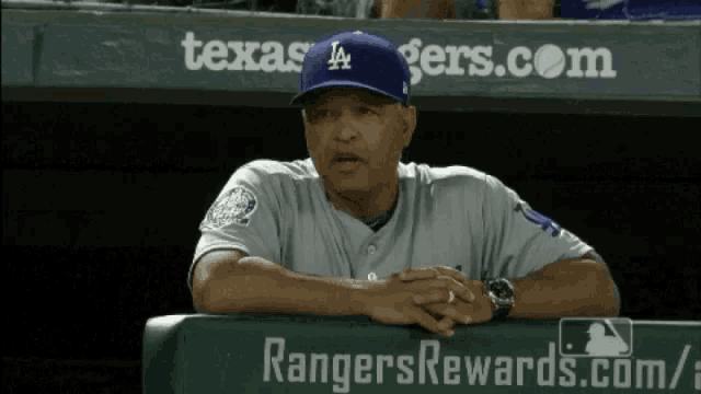 a man wearing a la hat sits on a dugout bench