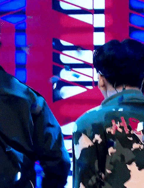 a man in a camouflage jacket is standing in front of a red and blue wall .