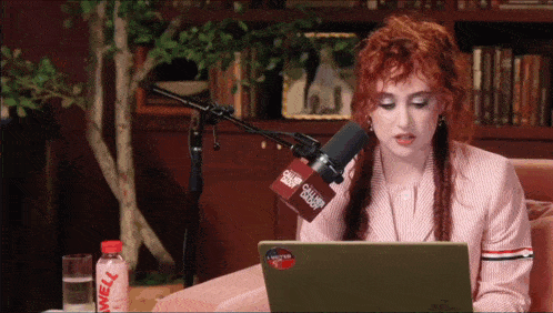 a woman is sitting in front of a microphone with a sticker on her laptop that says " i voted "