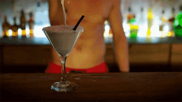 a martini glass with a straw and a man behind it