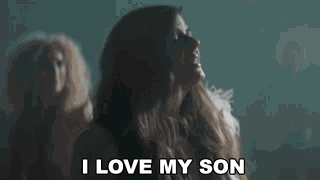 a woman is dancing in a dark room and saying `` i love my son '' while another woman looks on .