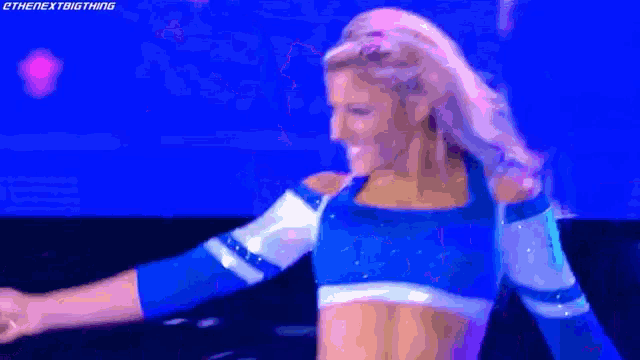 a woman in a blue and white crop top is dancing on a stage with her arms outstretched .