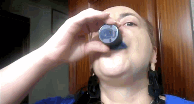 a woman in a blue shirt is drinking from a bottle that says ' coca cola ' on it